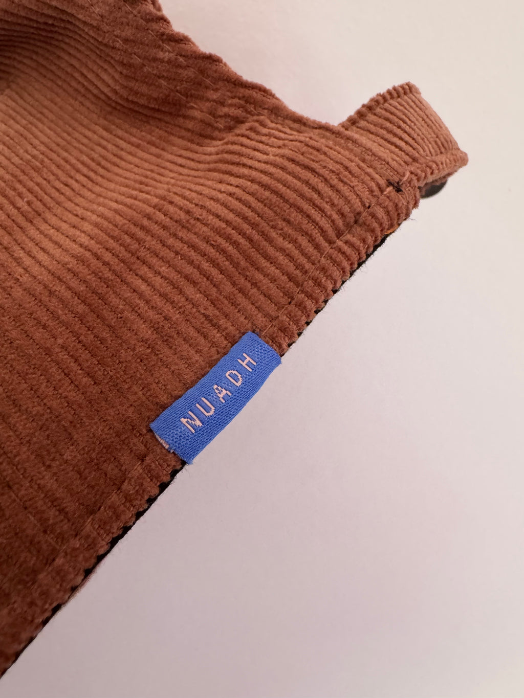 close up of NUADH DENIM - Sannox bay 6 panel surfer cap - cord fabric -  Pink - redwood colour with tonal lighter rose NUADH denim logo embroidery.