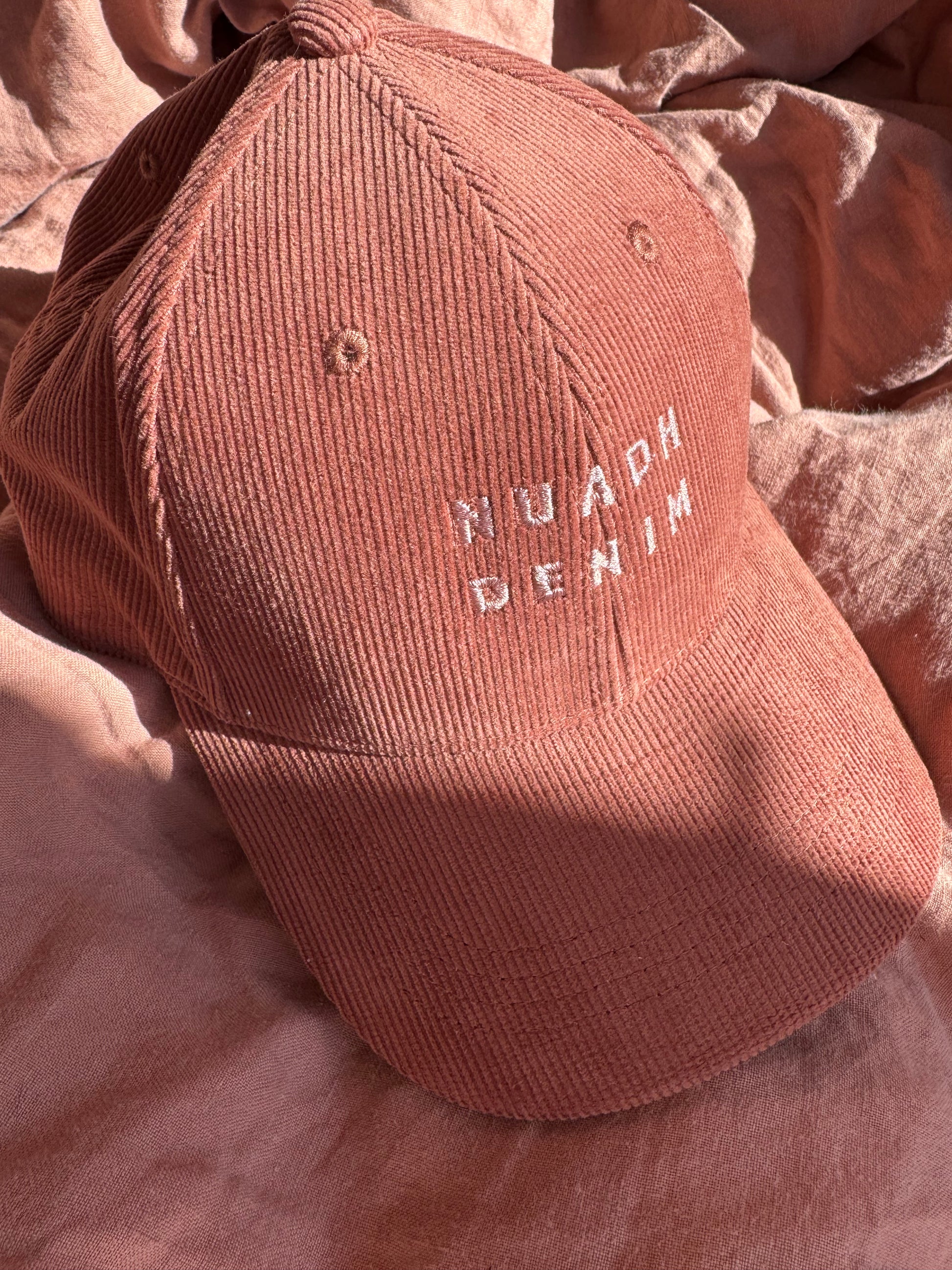 close up of NUADH DENIM - Sannox bay 6 panel surfer cap - cord fabric -  Pink - redwood colour with tonal lighter rose NUADH denim logo embroidery.
