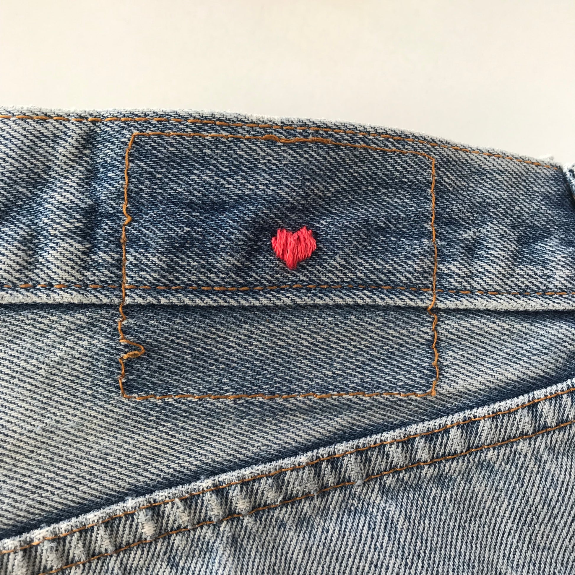 a waist band of vintage jeans curated by NUADH DENIM with a tiny pink love heart hand embroidery where the leather patch is missing.