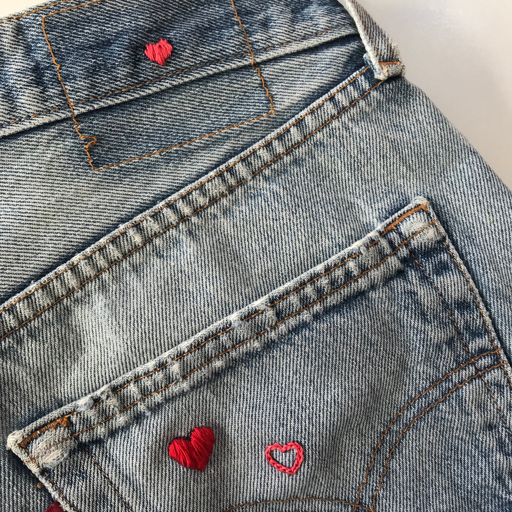 a waist band of vintage jeans curated by NUADH DENIM with a tiny pink love heart hand embroidery where the leather patch is missing and on the back pocket.