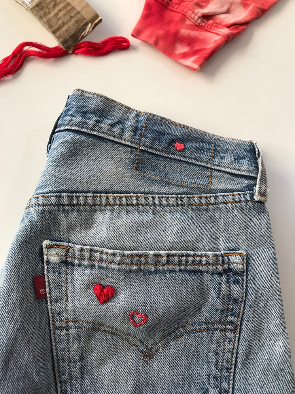 a waist band of vintage jeans curated by NUADH DENIM with a tiny pink love heart hand embroidery where the leather patch is missing and on the back pocket.